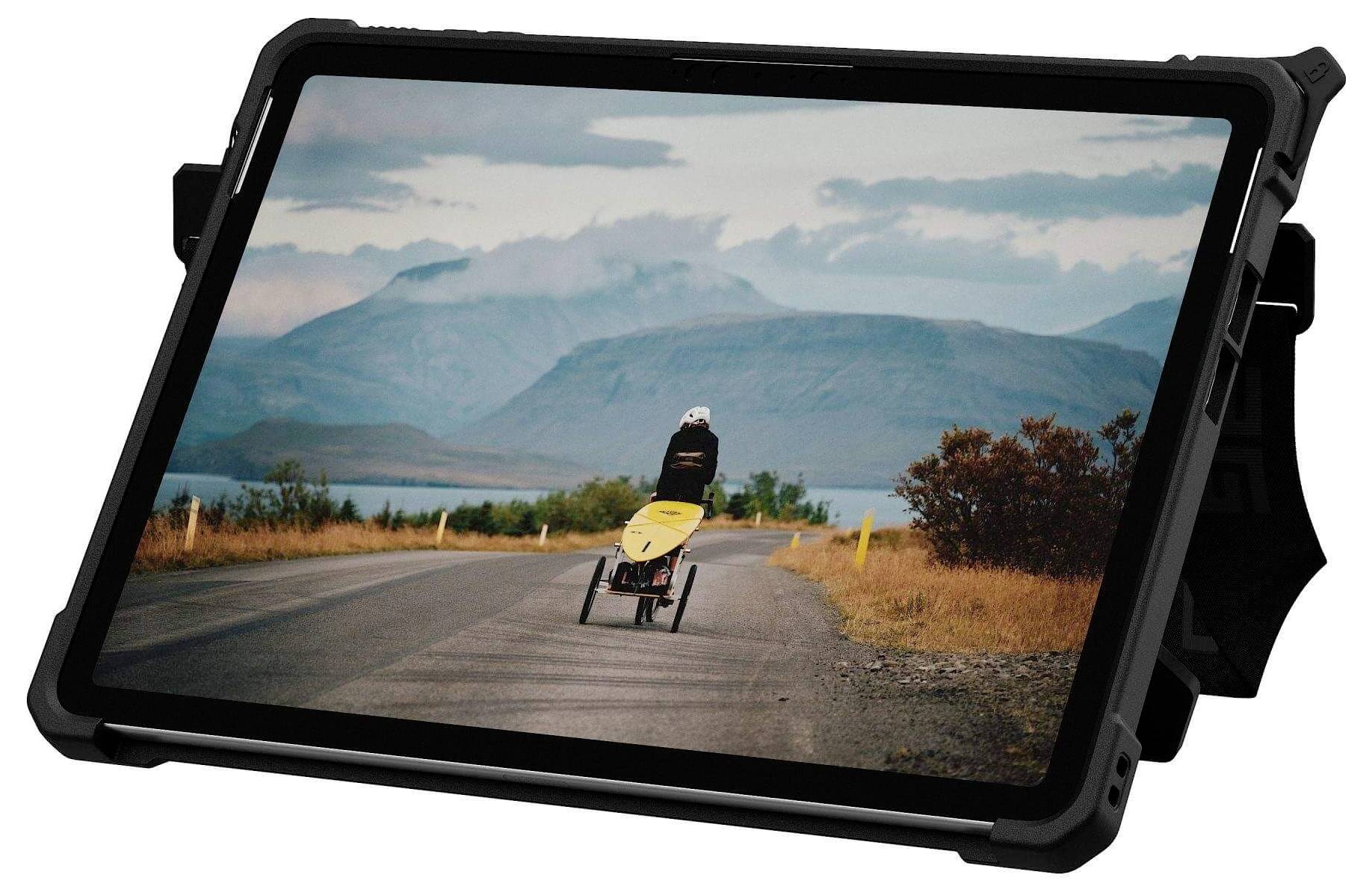 Eine Person im Rollstuhl fährt auf einer leeren Straße auf Berge zu, unter einem bewölkten Himmel, was eine Reise oder ein Abenteuer andeutet.