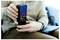 Person, die ein Smartphone mit einer Benachrichtigung über niedrigen Akkustand auf dem Bildschirm verwendet, sitzt drinnen, trägt einen beigen Pullover und braune Hose.
