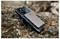 Ein Smartphone mit einer Schutzhülle und einem schlanken Metallbrieftasche, die daran befestigt ist, ruht auf einer felsigen Oberfläche im Freien.