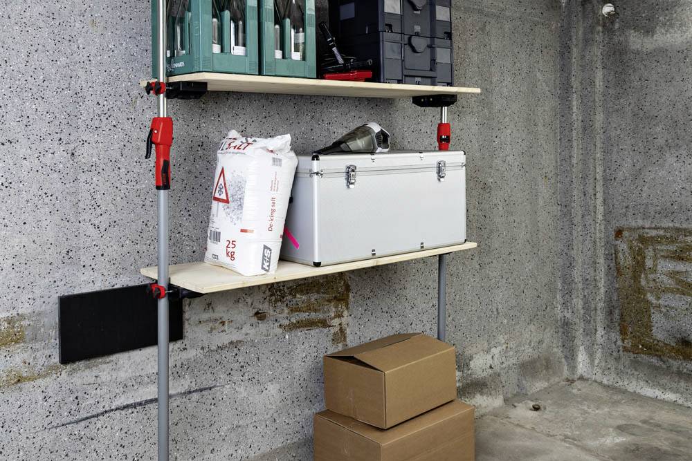 Eine Garage mit Regalen, auf denen Werkzeugkästen stehen, ein Sack Mörtel und ein Metallkoffer. Zwei Pappkartons sind auf dem Boden gestapelt.