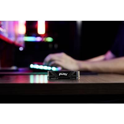 Ein Computerenthusiast verwendet eine beleuchtete Tastatur. Im Vordergrund liegt eine Kingston Fury Renegade SSD auf dem Schreibtisch.