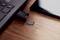 Ein Laptop mit einem USB-Kartenleser, der eingesteckt ist, mit einer microSD-Karte daneben auf einer Holzoberfläche und einem Smartphone in der Nähe.