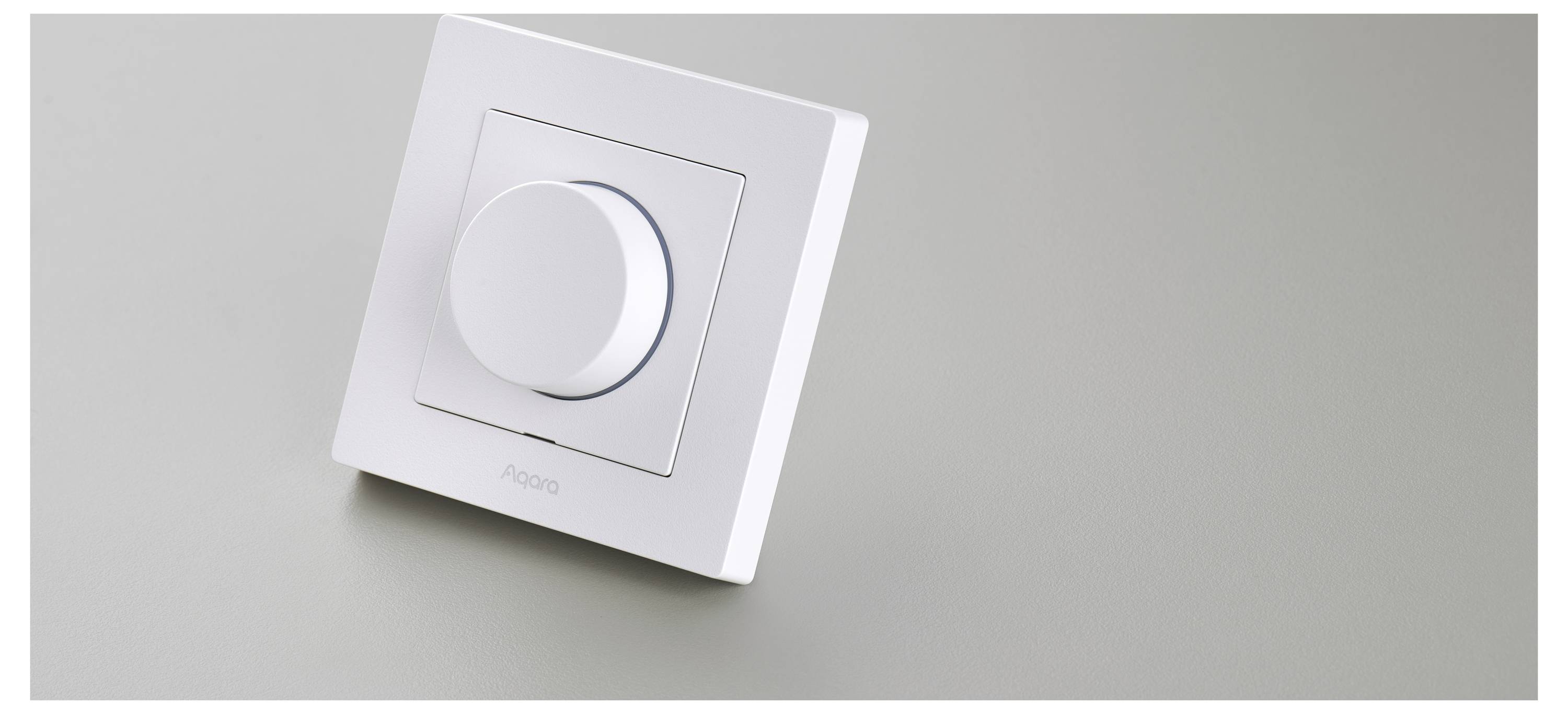 Ein weißer, wandmontierter Dimmer-Schalter mit rundem Drehregler, beschriftet mit 'Avato', ist zentriert auf einer glatten, hellgrauen Oberfläche angebracht.