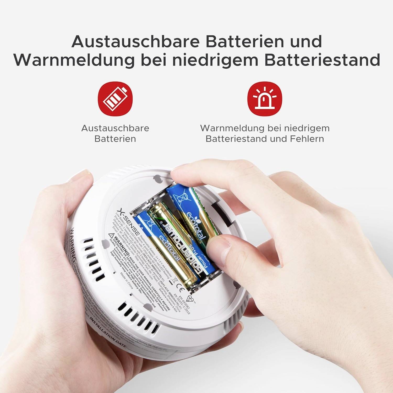Ein Rauchmelder wird mit zwei AA-Batterien bestückt. Text weist auf austauschbare Batterien und Warnung bei niedrigem Batteriestand hin.
