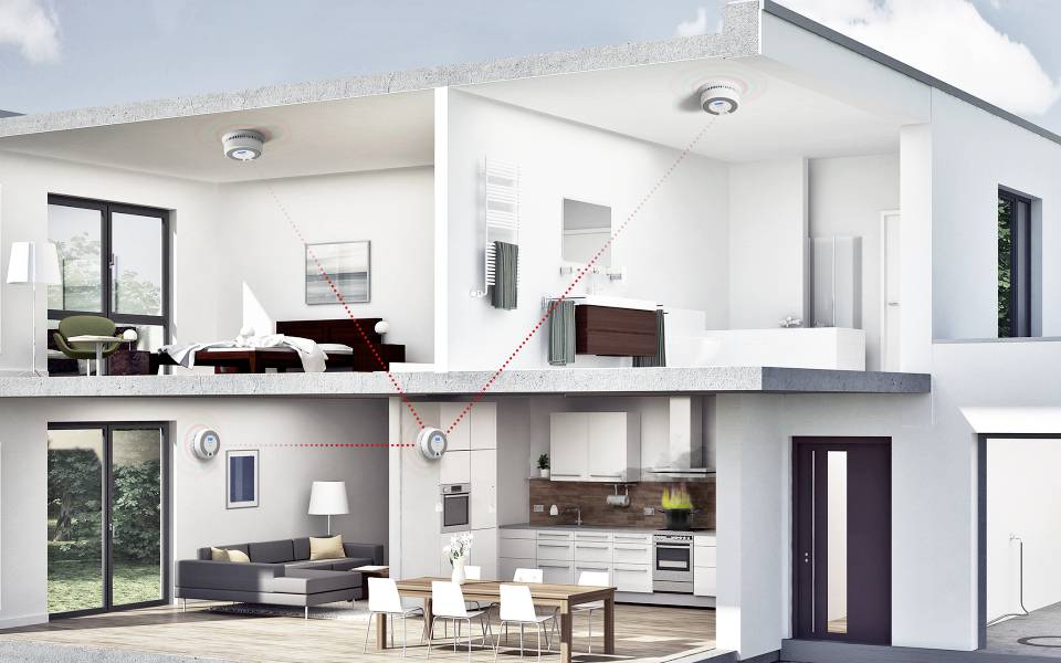 Schnittansicht eines modernen Zweistockhauses mit miteinander verbundenen Rauchmeldern im Wohnzimmer, in der Küche und in den Schlafzimmern.