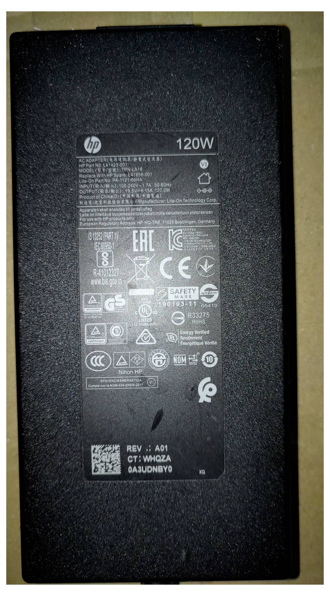 Ein schwarzer HP 120W Netzteil mit verschiedenen Zertifizierungslogos, Sicherheitsinformationen und Modelldetails, die in weißer Schrift gedruckt sind.