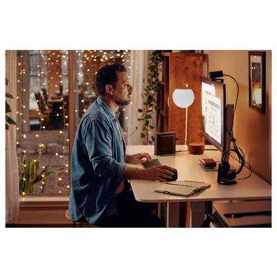 Ein Mann sitzt an einem Schreibtisch und arbeitet an einem Computer, konzentriert auf den Bildschirm, der eine Präsentation zeigt. Warmes Licht und Lichterketten schaffen eine gemütliche Atmosphäre.