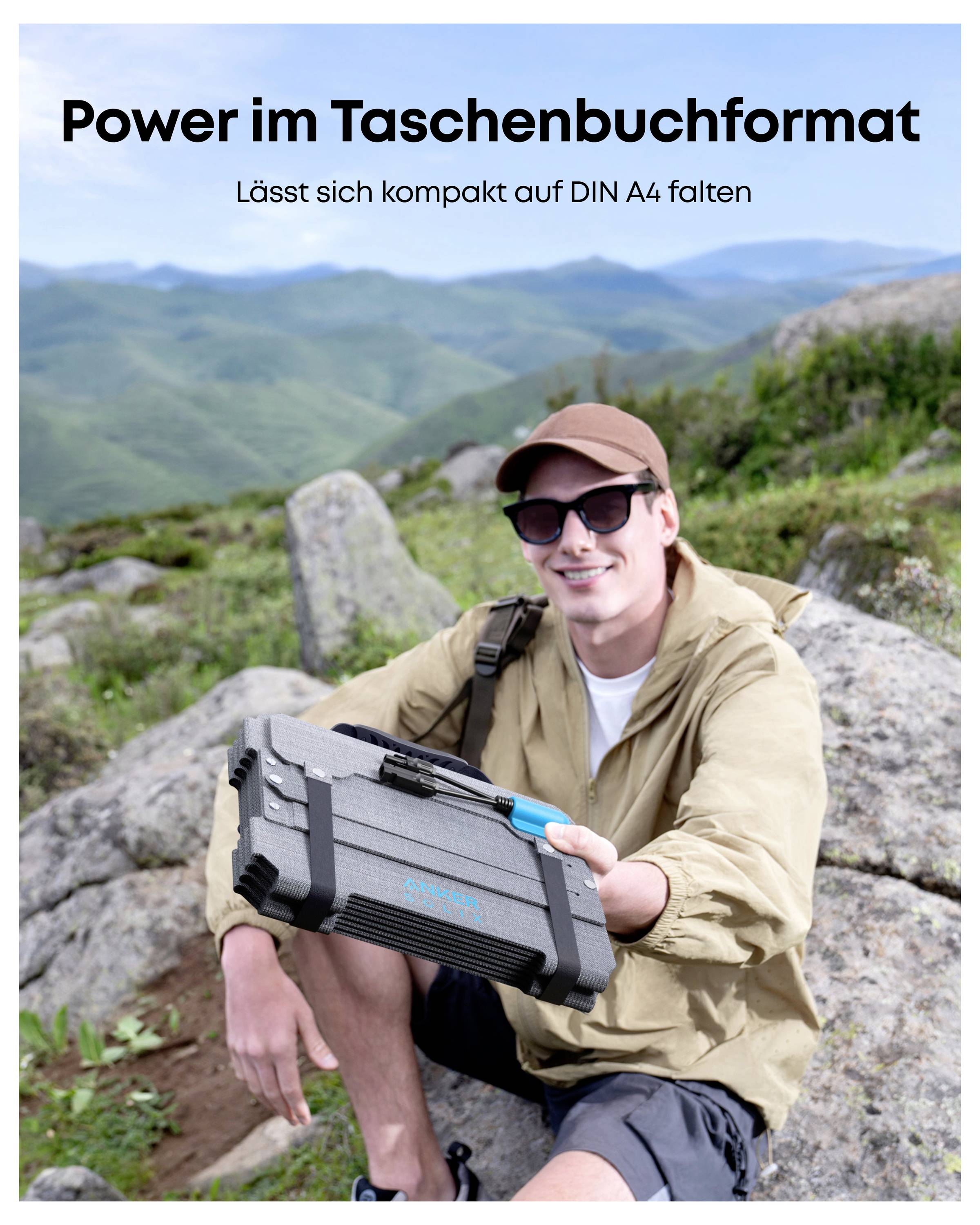 A person sits on a grassy hill with mountains in the background, holding a small, portable power device. The text reads 'Power im Taschenbuchformat. Lässt sich kompakt auf DIN A4 falten.'<br><br>The text is already in German, so no translation is needed.