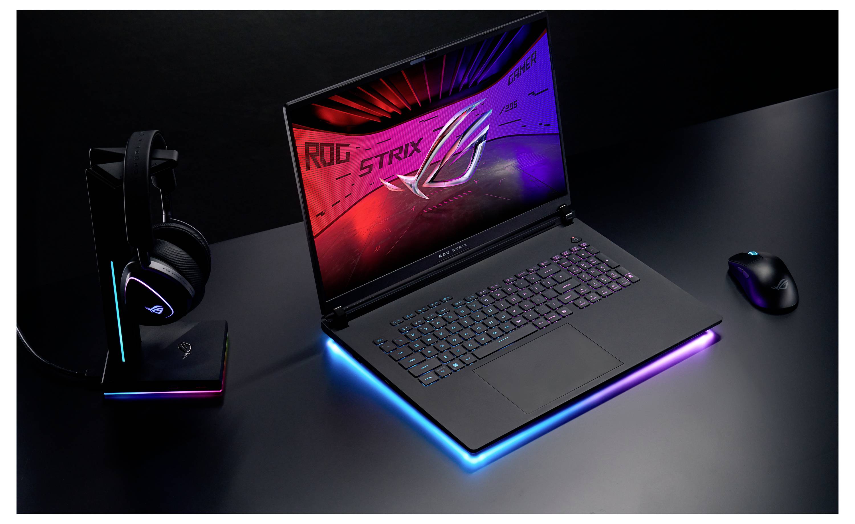 Ein Gaming-Laptop mit einer beleuchteten Tastatur zeigt das ‚ROG STRIX' Logo auf seinem Bildschirm. Kopfhörer und eine Maus sind in der Nähe platziert.