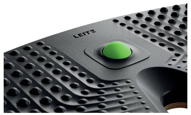 Ein strukturiertes schwarzes Gerät mit einer auffälligen grünen Taste in der Mitte, mit der Aufschrift "Leitz", was wahrscheinlich auf eine Energie- oder Aktivierungsfunktion hinweist.