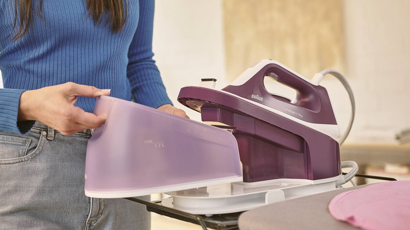 Eine Person in einem blauen Hemd befüllt ein lila Dampfbügeleisen in einem Waschraum.