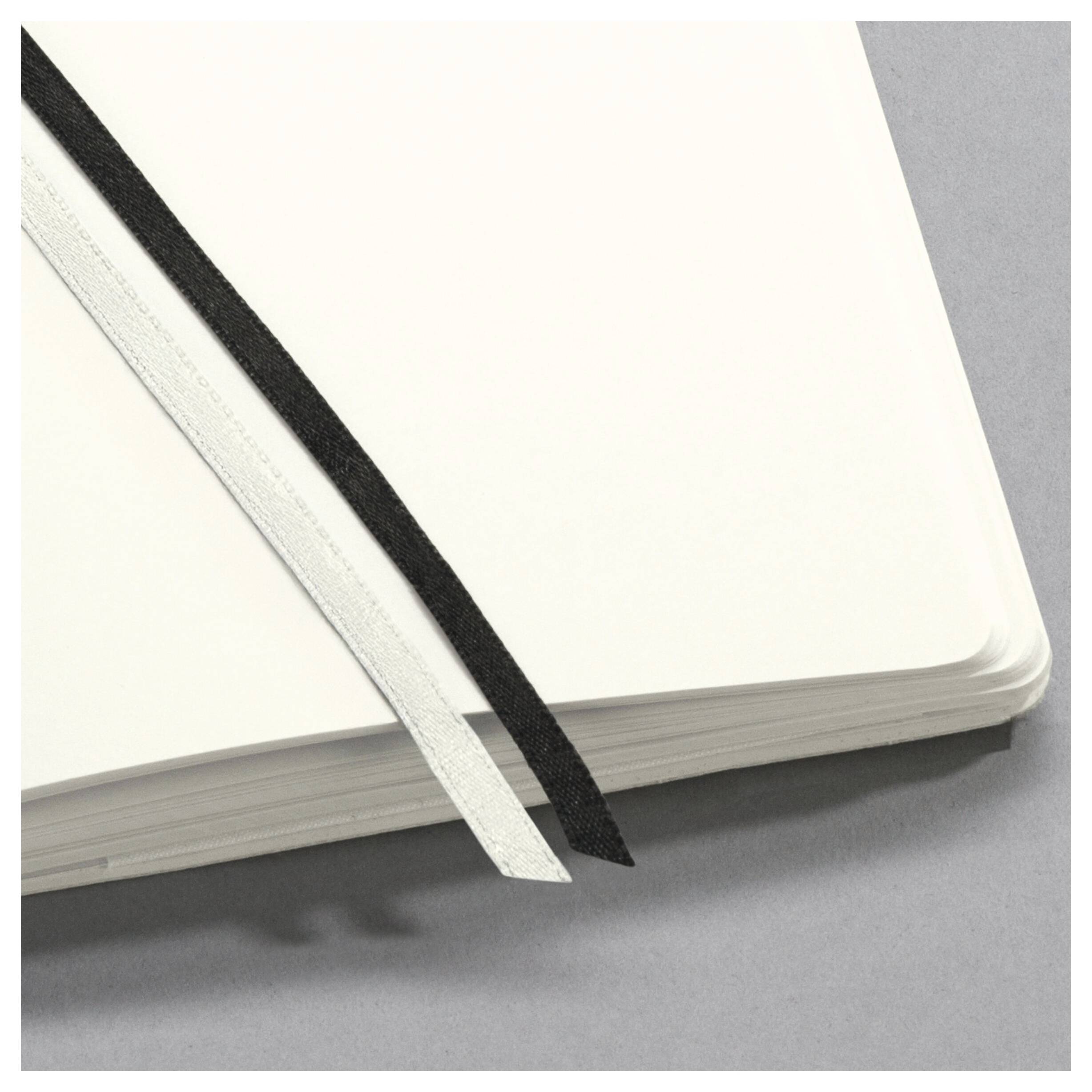 Notizbuch mit leeren weißen Seiten und zwei Lesezeichen, eines schwarz und eines weiß, diagonal über die Seiten gelegt.