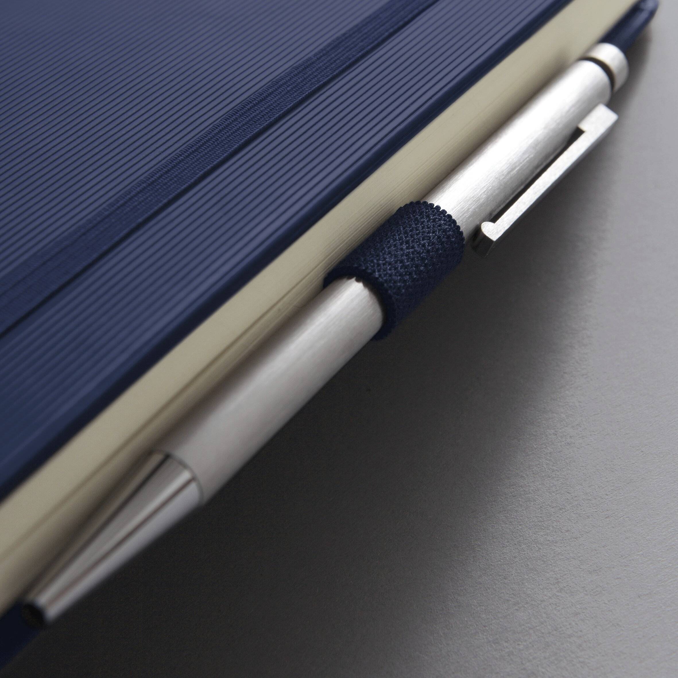 Ein silberner Stift ist an ein geschlossenes blaues Notizbuch geklippt und unterstreicht damit eine professionelle und organisierte Umgebung.