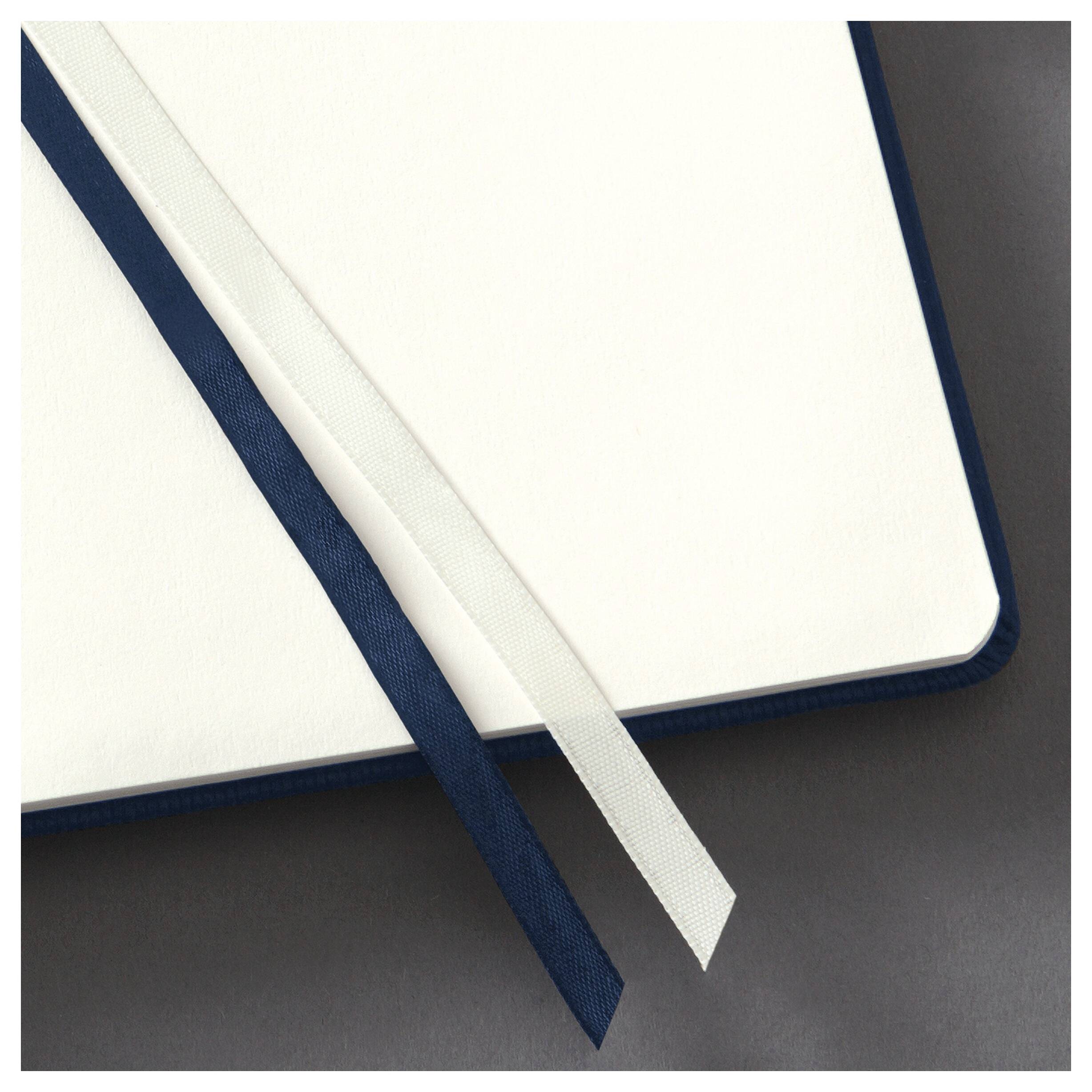 Ein Notizbuch mit blauer Umschlagseite liegt geöffnet auf einer grauen Oberfläche. Zwei Lesezeichen, eines weiß und eines blau, liegen diagonal über den leeren Seiten.