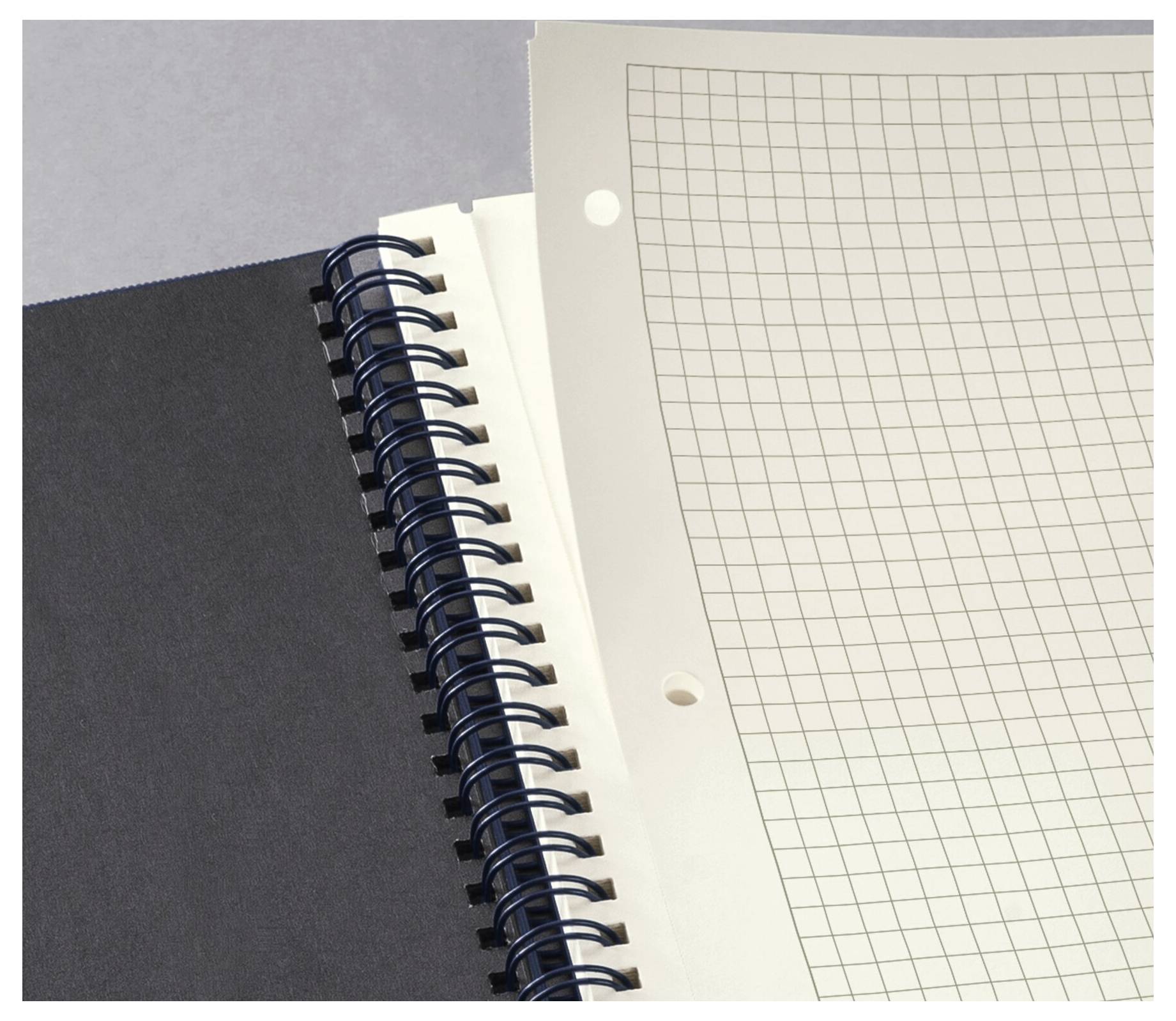 Ein Spiralblock mit schwarzer Umschlagseite ist geöffnet und zeigt Millimeterpapier im Inneren.