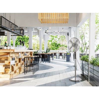 Ein Straßencafé mit Holzeinrichtung, hohen Hockern und einem Deckenventilator. Umgeben von Grünpflanzen, bietet es eine entspannte und luftige Atmosphäre.
