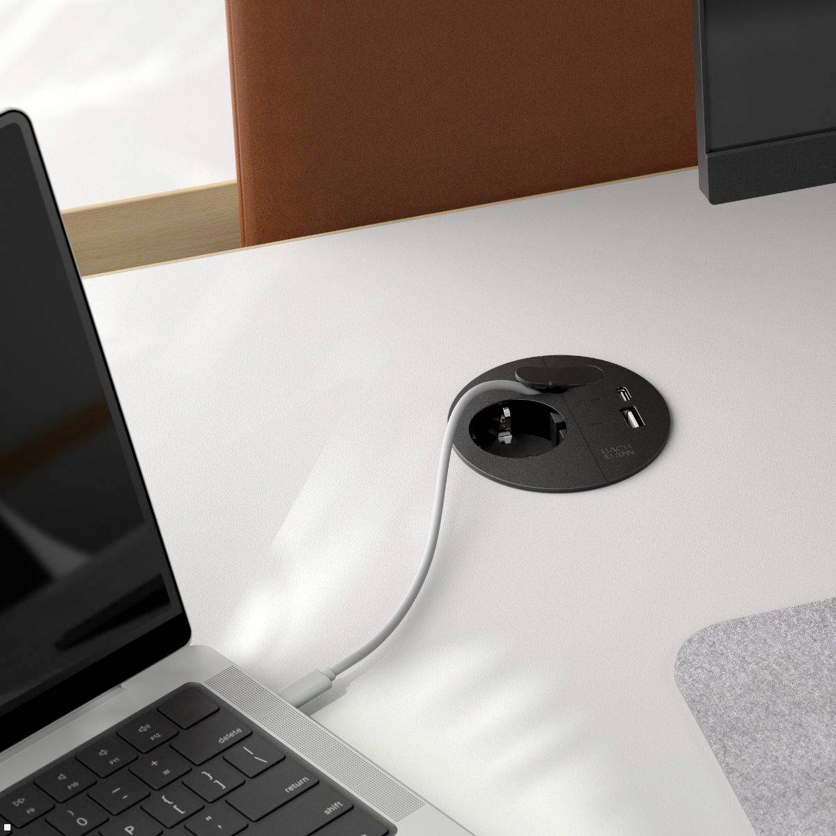 Ein aufgeräumter Büroschreibtisch mit einem Laptop, einem Kabel, das mit einer Steckdose verbunden ist, und einem roten Notizbuch, der einen ordentlichen und organisierten Arbeitsplatz vermittelt.