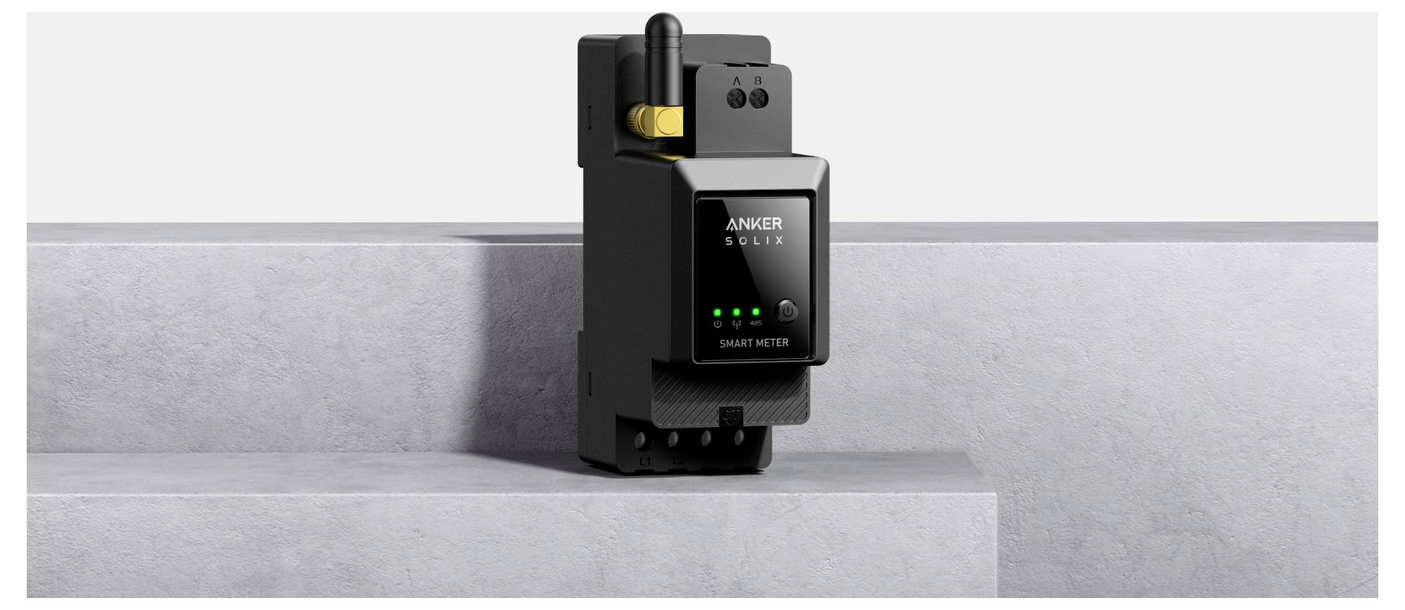 Ein schwarzer Anker Solix Smart Meter mit digitalem Display und grünen Anzeigelichtern ist auf einer grauen Betonoberfläche montiert.