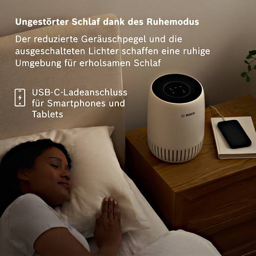 Eine Frau schläft ruhig in einem Bett. Neben ihr auf einem Nachttisch steht ein Luftreiniger mit einem Smartphone und Ladegerät.