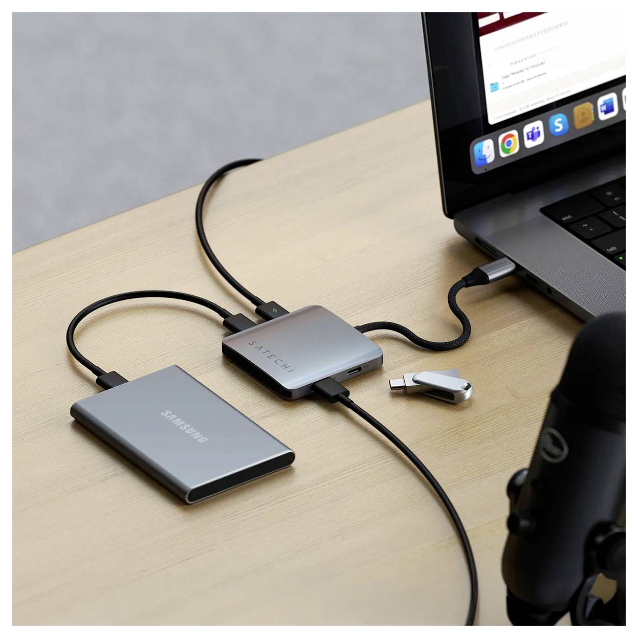 Ein Laptop, der mit einem USB-C-Hub mit mehreren Anschlüssen verbunden ist und an eine externe Festplatte sowie ein Mikrofon angeschlossen ist, was Datenübertragung und Aufnahme andeutet.