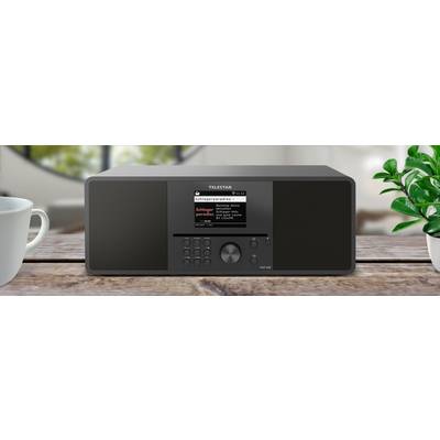 Ein schwarzes TELESAR Digitalradio steht auf einem Holztisch mit einer Anzeige, die ‚Schlagerparadies' zeigt, umgeben von einer Tasse und einem Fensterblick.