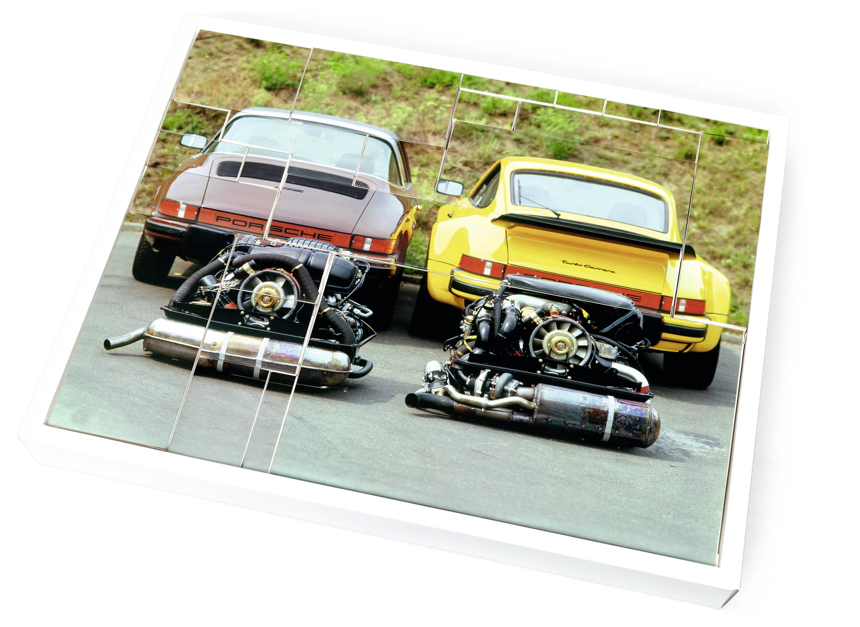 Zwei Oldtimer, ein roter und ein gelber Porsche, stehen rückwärts eingeparkt. Zwei Motoren sind auf dem Boden in der Nähe ausgestellt und zeigen mechanische Details.