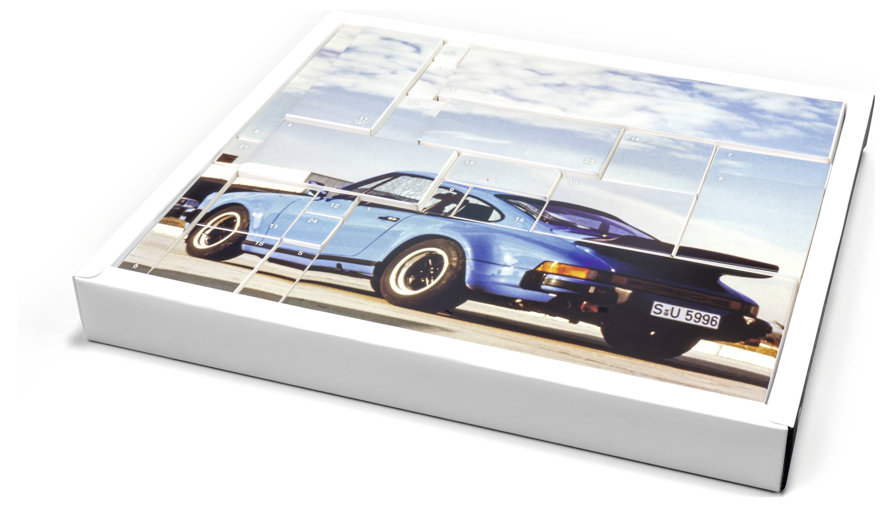 Eine Puzzlebox mit einem Bild eines klassischen blauen Sportwagens auf einer Küstenstraße unter einem klaren Himmel.