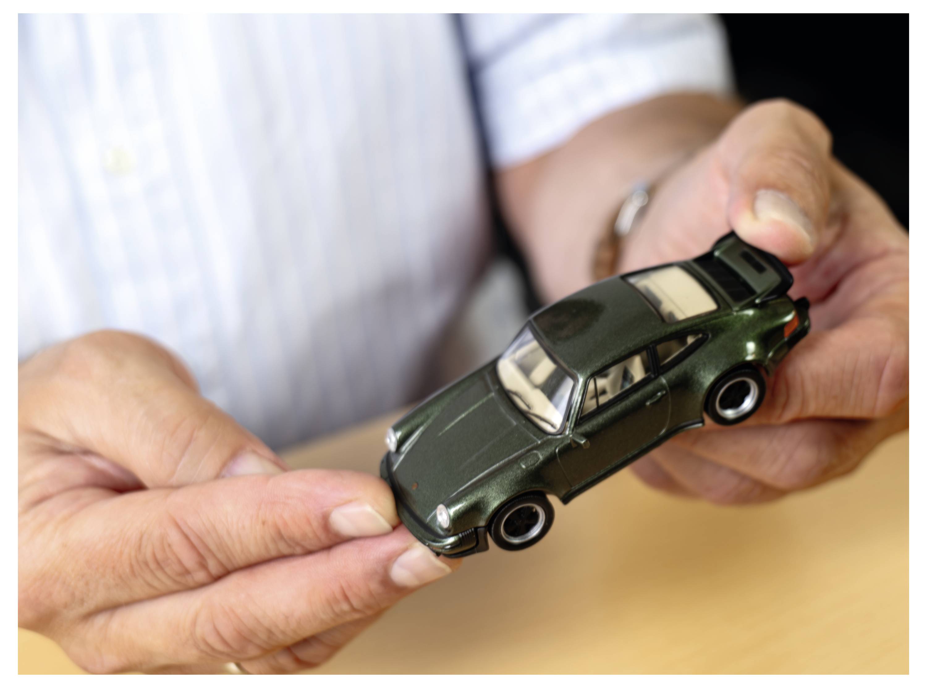 Eine Person hält ein kleines dunkelgrünes Spielzeugauto mit beiden Händen und konzentriert sich auf die Details des Modells.