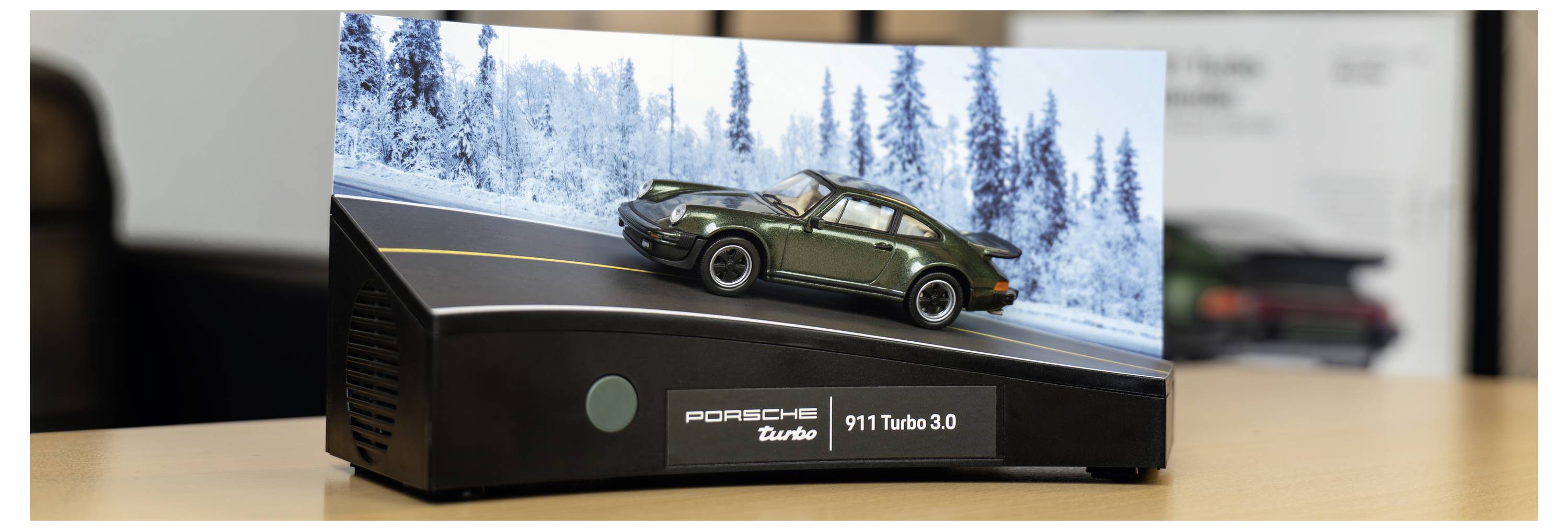 Ein Modell-Porsche-Auto auf einer geschwungenen, eisigen Straße mit schneebedeckten Bäumen im Hintergrund; beschriftet mit 'Porsche Turbo 911 Turbo 3.0'.