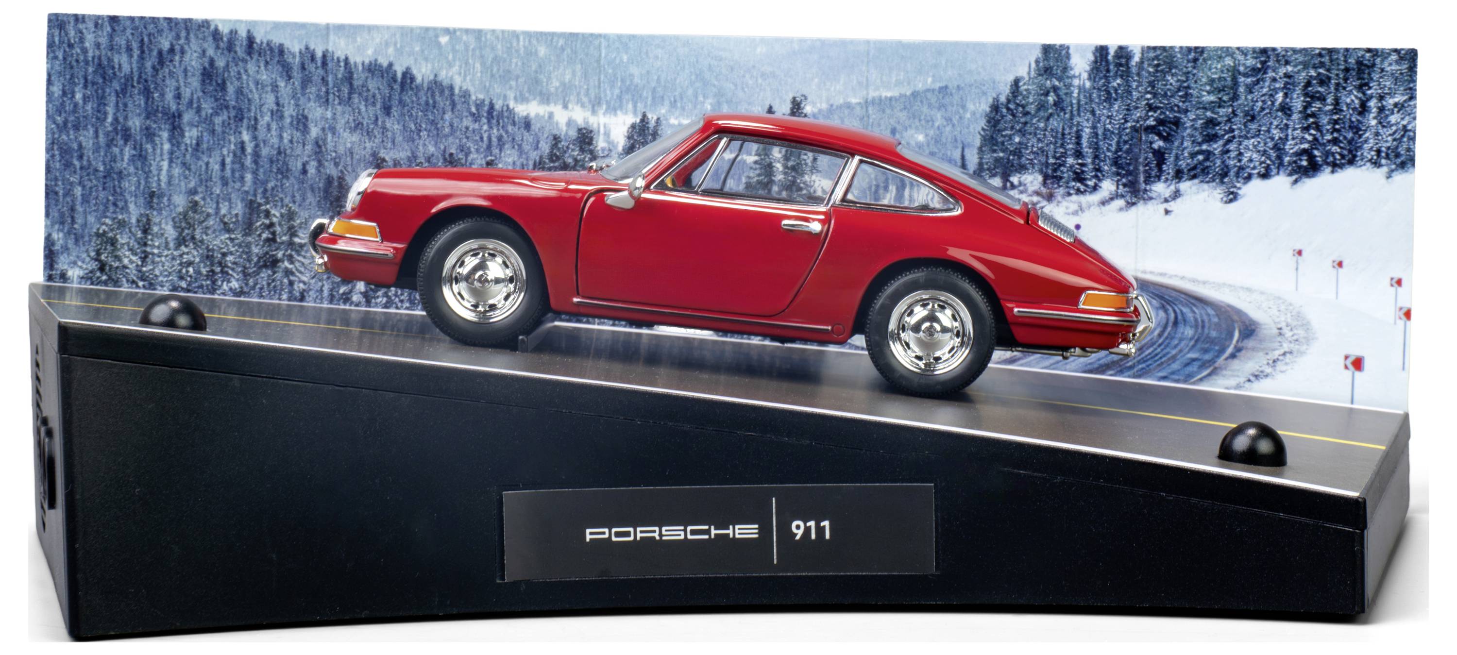 Ein Modell eines roten Porsche 911 ist auf einem Präsentationsständer montiert, vor einem verschneiten Waldhindergrund mit einer kurvenreichen Straße, wobei das Design des Autos besonders hervorgehoben wird.