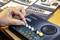 Eine Hand dreht einen Knopf auf einer kleinen Synthesizer-Platine mit der Beschriftung "SYNTHESIZER". Ein Handbuch mit Montageanweisungen ist auf dem Schreibtisch zu sehen.