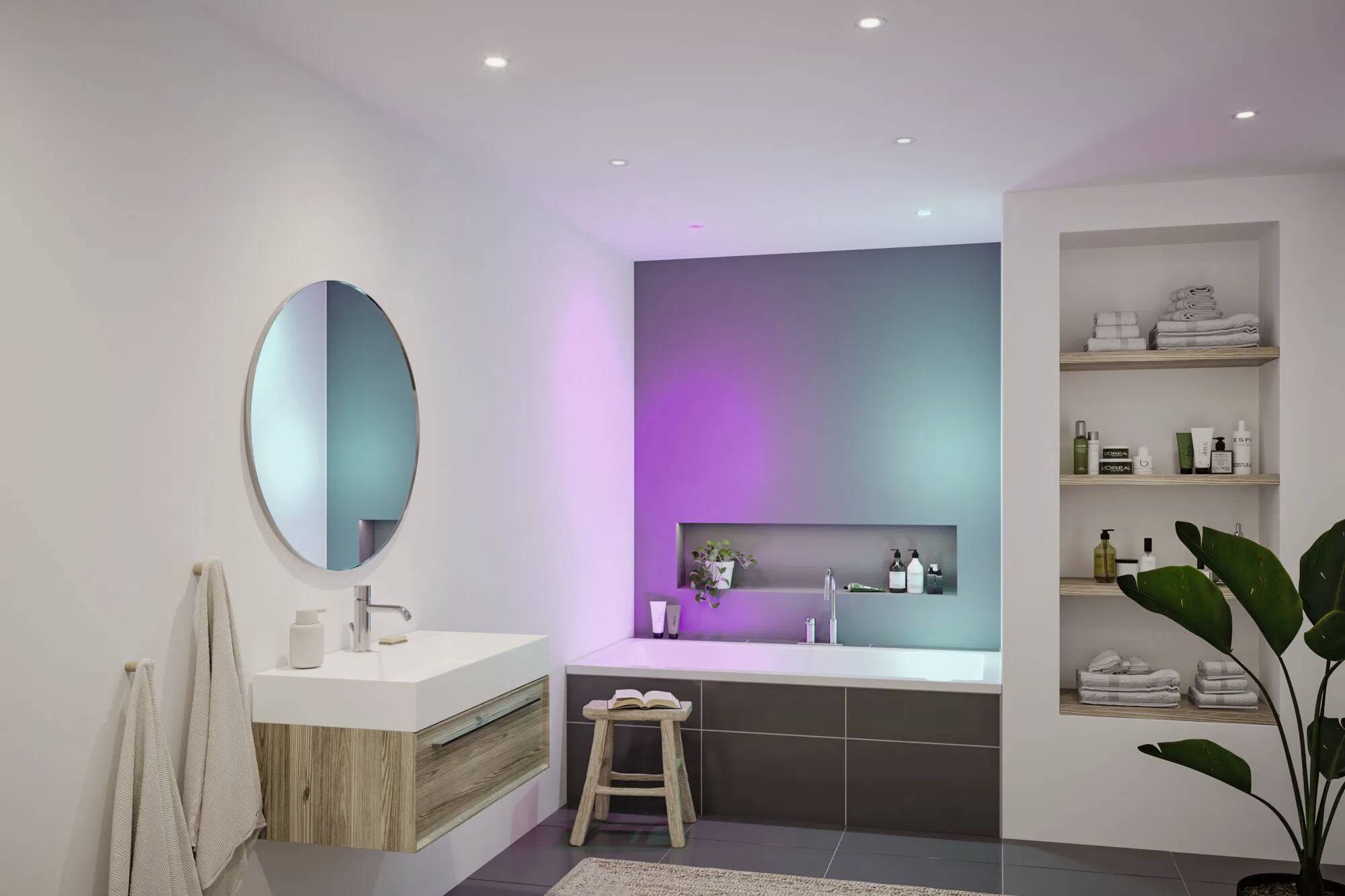 Ein modernes Badezimmer mit einer großen Badewanne, bunter LED-Beleuchtung und schwebenden Regalen. Ein rundes Spiegel und ein minimalistisches Waschbecken befinden sich auf der linken Seite.