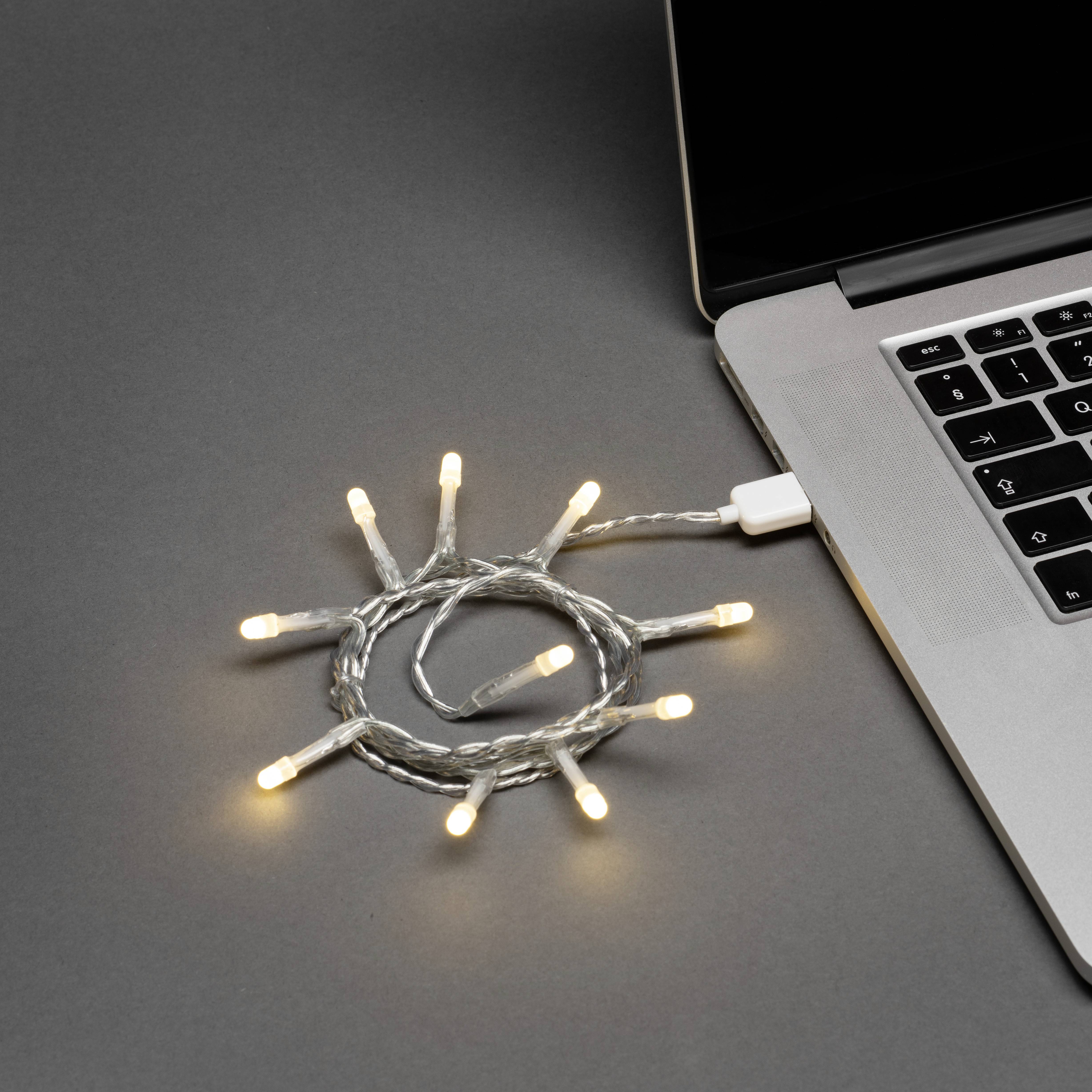 Lichterketten, die an einen Laptop angeschlossen sind, erzeugen ein helles, kreisförmiges Muster auf einer dunklen Oberfläche und deuten auf Kreativität oder festliche Stimmung hin.