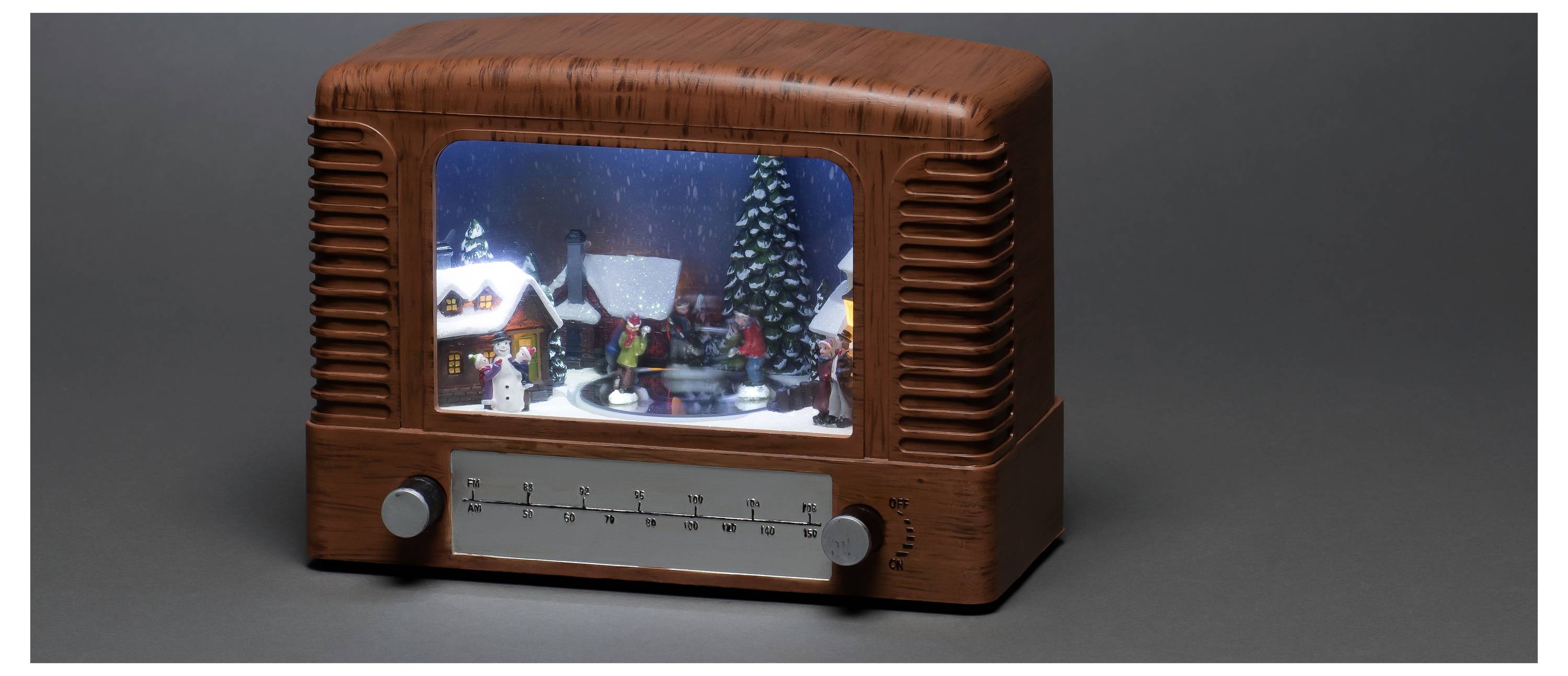 Ein im Vintage-Stil gehaltenes Radio mit einer Winterdorfszene im Display, die Schnee, Häuser und Figuren vor einem dunklen Hintergrund zeigt.