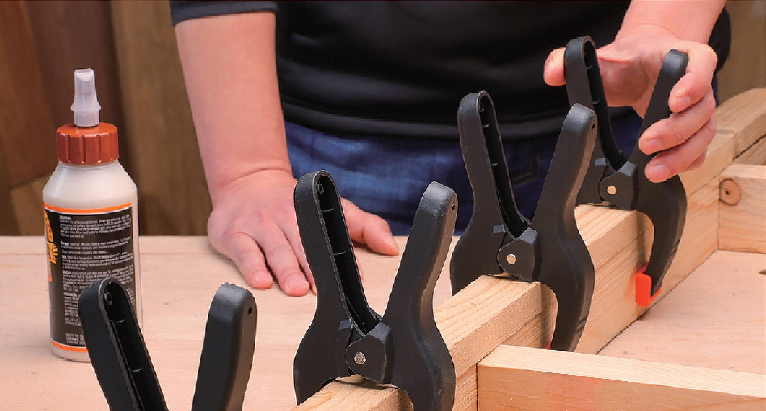 Eine Person, die einen Holzrahmen mit Schraubzwingen und Holzleim zusammenbaut und sich dabei auf den Konstruktionsprozess konzentriert.