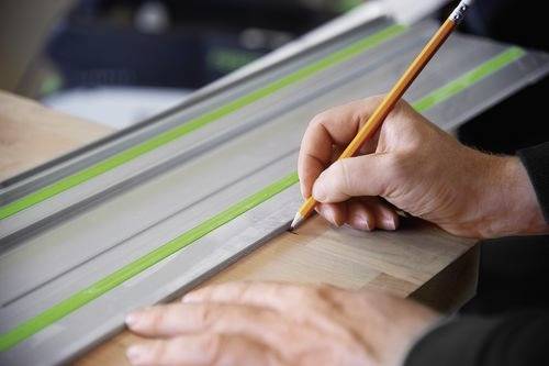 Eine Person verwendet einen Bleistift und ein Metalllineal, um eine gerade Linie auf einem Stück Holz zu ziehen und damit eine präzise Messung und Planung anzuzeigen.