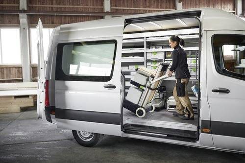 Eine Person organisiert und lädt Ausrüstung in einen weißen Lieferwagen in einem Lagerhaus und bereitet sich auf den Transport oder einen Auftrag vor.