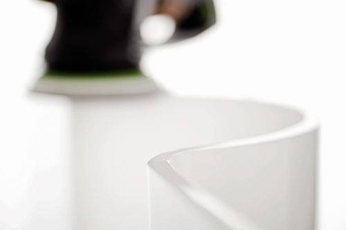 Eine Nahaufnahme eines Elektrowerkzeugs, das die Kante einer gebogenen, weißen Oberfläche schleift und einen glatten Finish bearbeitet.