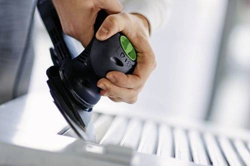 Eine Person benutzt einen tragbaren elektrischen Schleifer auf einer Holzoberfläche und glättet das Material mit Präzision.