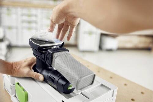 Eine Hand demonstriert das Anbringen eines Staubbeutels an einem kompakten Schleifer auf einer Werkbank und betont dabei Benutzerfreundlichkeit und Praktikabilität.