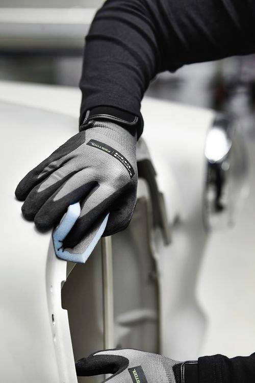 Eine Person mit Handschuhen reinigt den Rand einer weißen Oberfläche, möglicherweise eines Autos, mit einem blauen Tuch und legt dabei Wert auf Präzision.