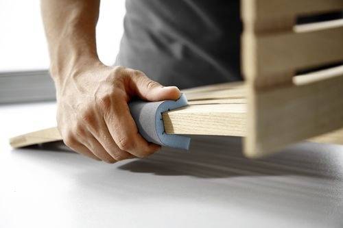 Eine Person, die Holzlatten unter Verwendung eines blauen Schaumstofftrenners auf einer flachen Oberfläche zusammenbaut.