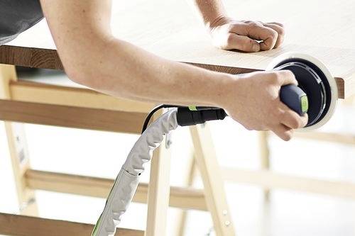 Eine Person schleift eine Holzoberfläche mit einem elektrischen Handschleifer und demonstriert dabei einen Holzbearbeitungsprozess.
