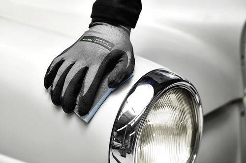 Eine behandschuhte Hand poliert die Motorhaube eines Oldtimers in Weiß und konzentriert sich dabei auf einen glänzenden Chromscheinwerfer.