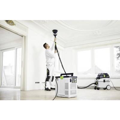 Eine Person in weißer Arbeitskleidung bedient einen Deckenschleifer, der an ein Vakuumsystem angeschlossen ist. Der Raum ist geräumig mit großen Fenstern im Hintergrund.