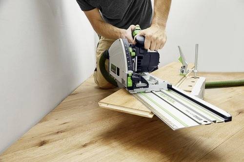 Eine Person verwendet eine Kreissäge, um Holzbretter auf einem Boden zu schneiden und nutzt dabei eine grüne Führungsschiene für Präzision.