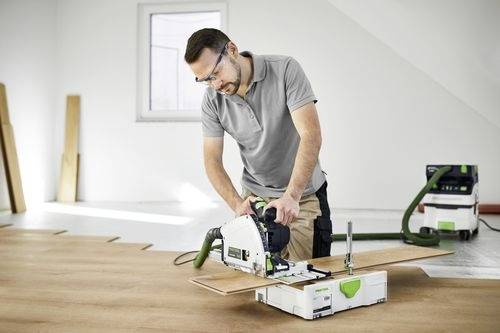 Eine Person mit Sicherheitsbrille verwendet eine Kreissäge, um Holzbretter in einer Werkstatt zu schneiden. Ein Staubsaugsystem sammelt den Staub.