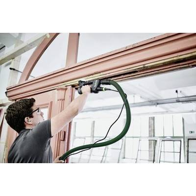 Eine Person verwendet ein Elektrowerkzeug, um einen Türrahmen zu schleifen, wobei ein grüner Schlauch zur Staubabsaugung angeschlossen ist, in einem hell erleuchteten Raum mit großen Fenstern.