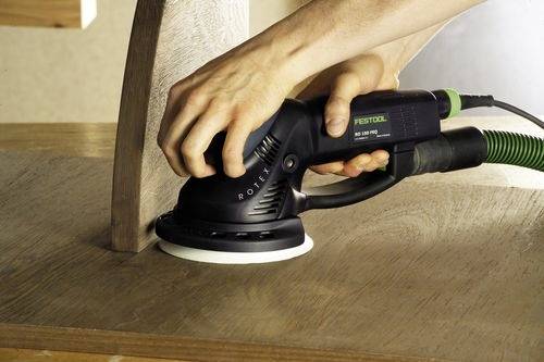 Eine Person schleift eine Holzoberfläche mit einem Festool-Elektroschleifer. Der Schleifer ist in Kontakt mit dem Holz und glättet die Maserung.