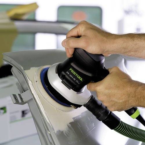 Eine Person verwendet eine elektrische Schleifmaschine von Festool an einem grauen Fahrzeugkotflügel und glättet die Oberfläche.